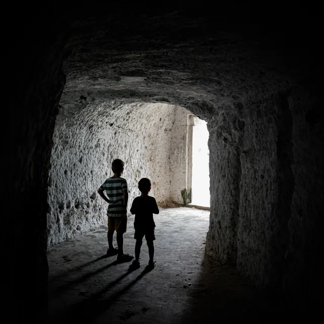 Two silhouetted figures walk toward daylight at the end of a rough stone passage.