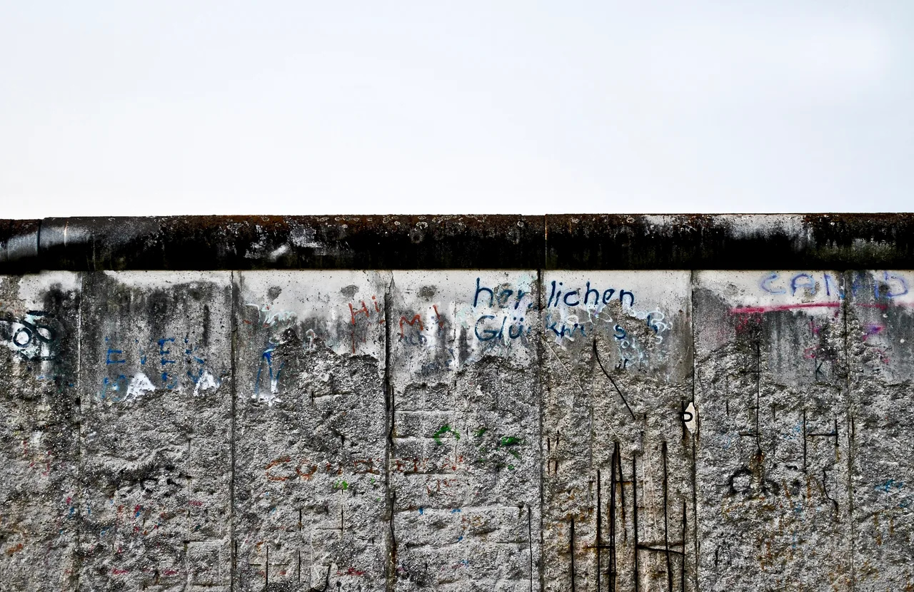 A long weathered concrete barrier with faded graffiti divides a pale sky from a dark foreground.