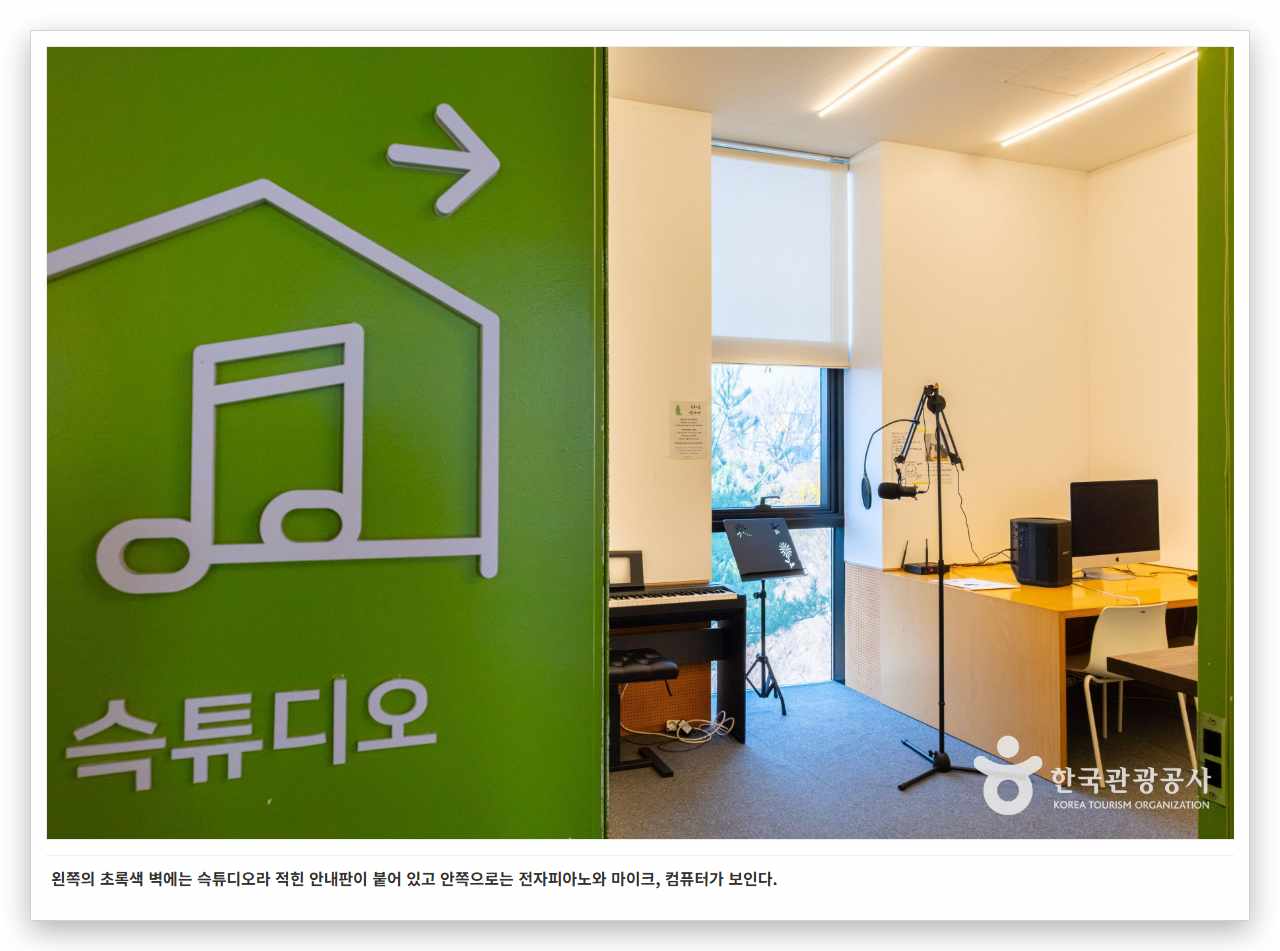 왼쪽의 초록색 벽에는 슥튜디오라 적힌 안내판이 붙어 있고 안쪽으로는 전자피아노와 마이크, 컴퓨터가 보인다.