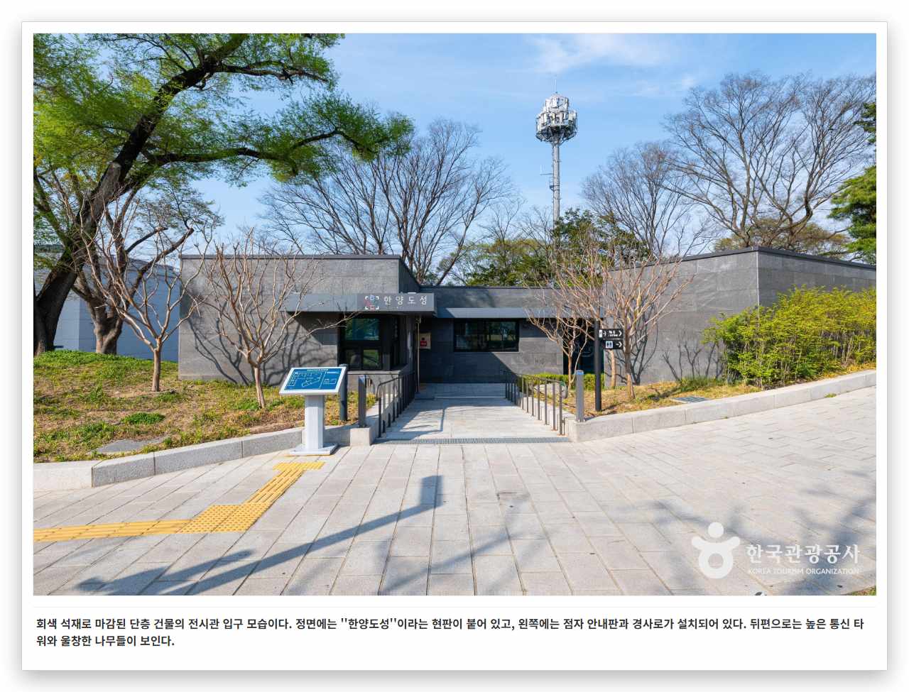 회색 석재로 마감된 단층 건물의 전시관 입구 모습이다. 정면에는 ''한양도성''이라는 현판이 붙어 있고, 왼쪽에는 점자 안내판과 경사로가 설치되어 있다. 뒤편으로는 높은 통신 타워와 울창한 나무들이 보인다.