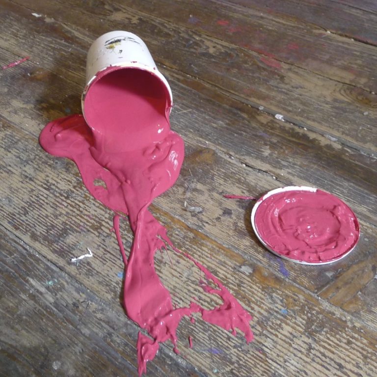 Un pot d'encre rose tombé au sol, qui se déverse en partie sur un vieux parquet en bis tâché