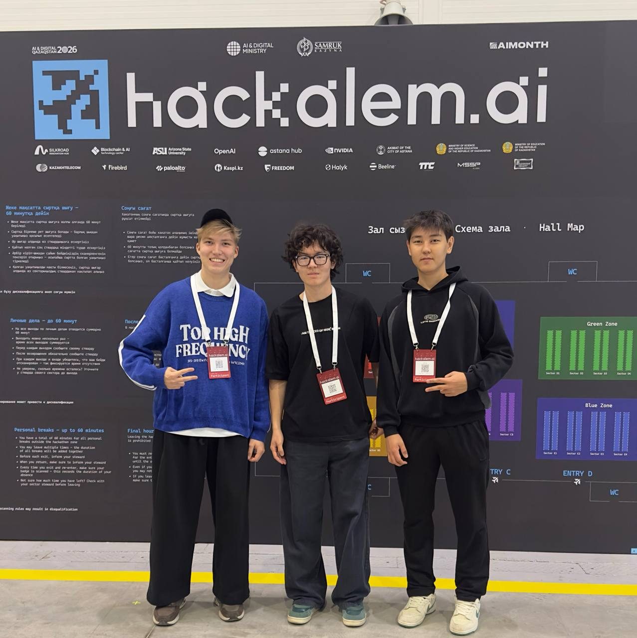 Team Plus, all three members, in front of the HackAlem AI wall