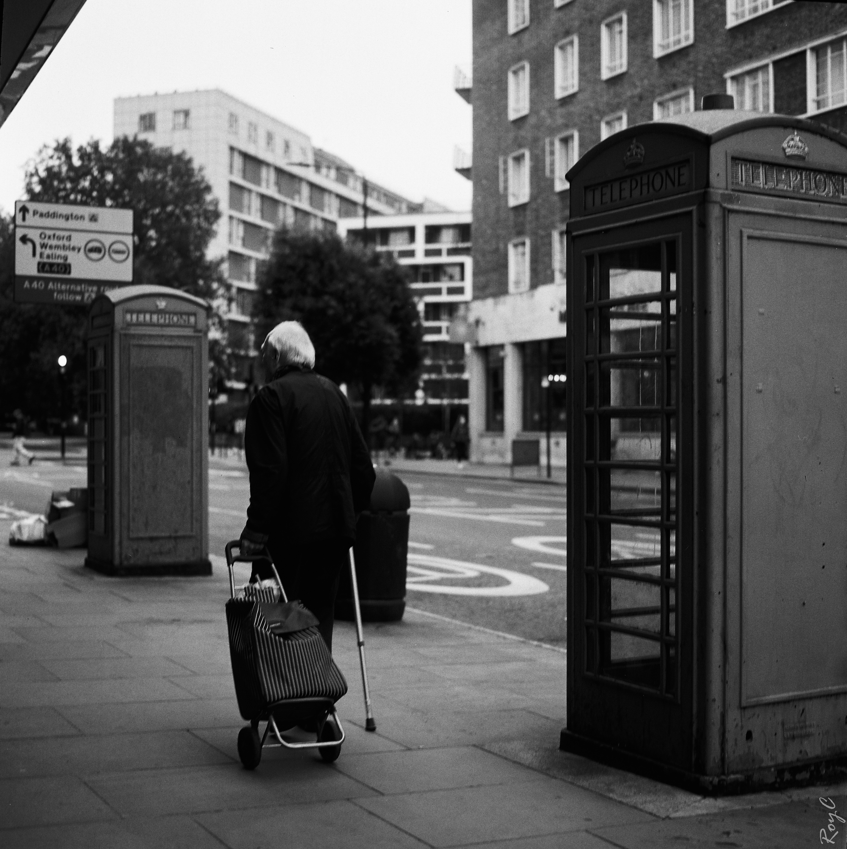 An Old Man Walking between two Telephone Boxes