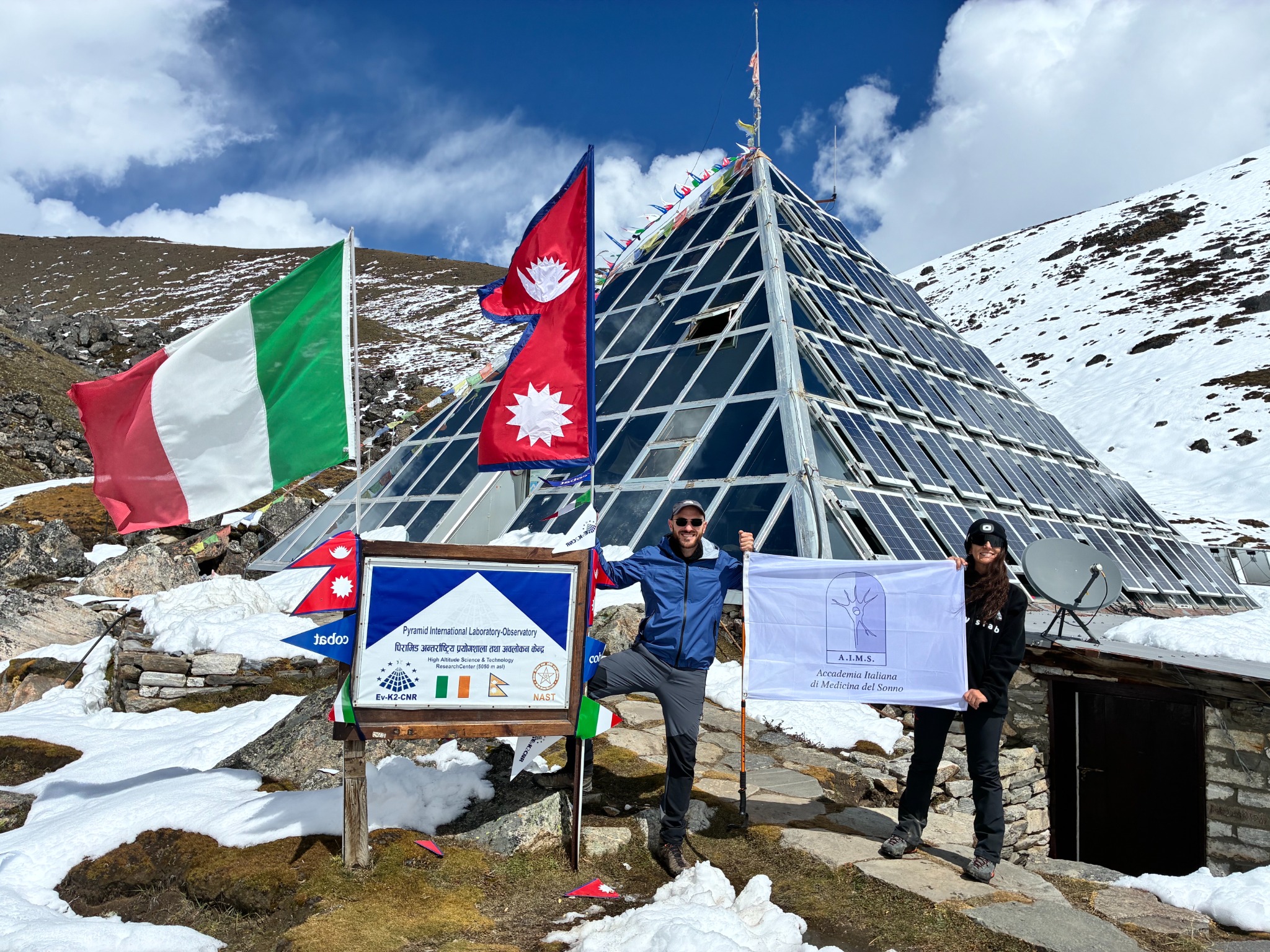Partecipanti a PYRAMID26 davanti al Laboratorio-Osservatorio Piramide in Nepal, con la bandiera AIMS
