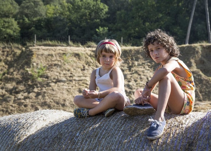 Dos niñas sentadas sobre una paca de paja en una tarde de verano en el campo. Fotograma de «Verano 1993» (Carla Simón, 2017).