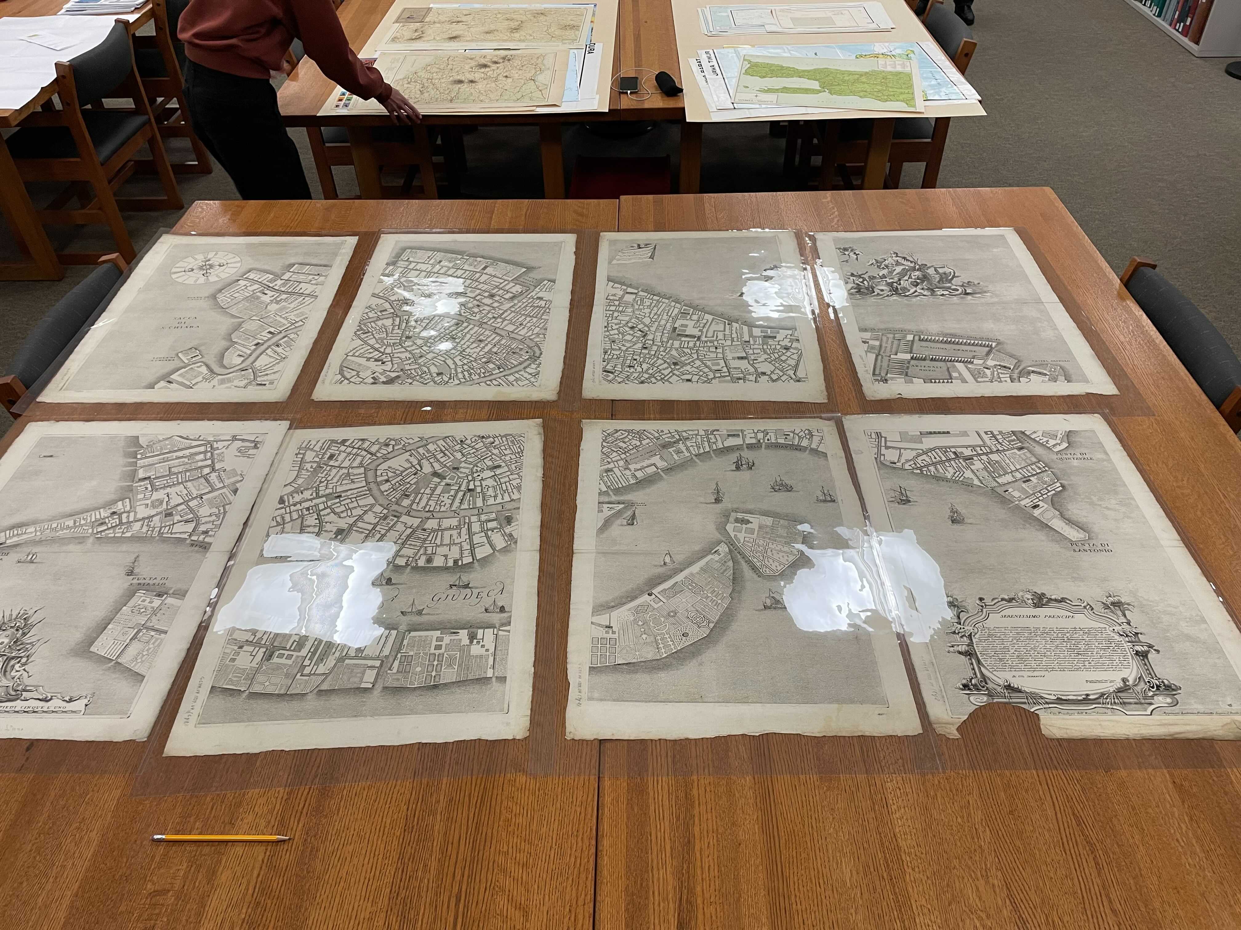 photograph of 8 historic map sheets laid out on a table in the map collection