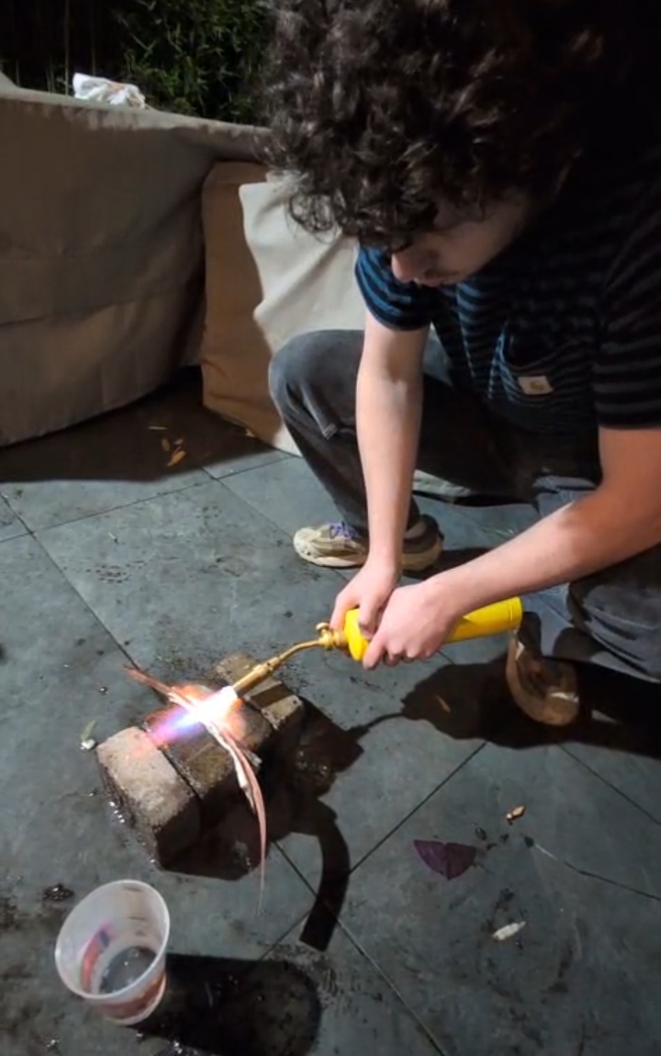 Annealing copper strips in the garden at night — gas torch flame on the copper, concrete block as a heat-resistant surface