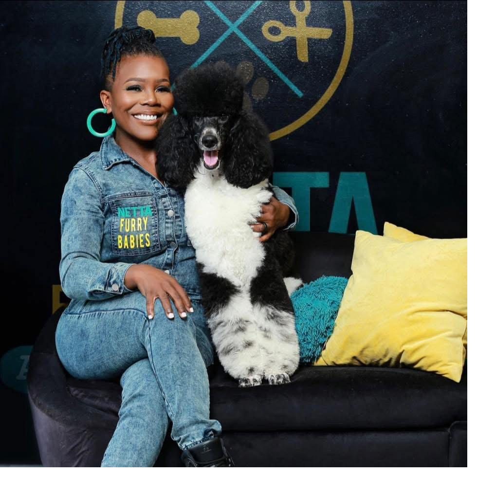 Johnette Wiggins seated with Dice the Doodle, her black-and-white standard poodle, in the Netta Furry Babies studio