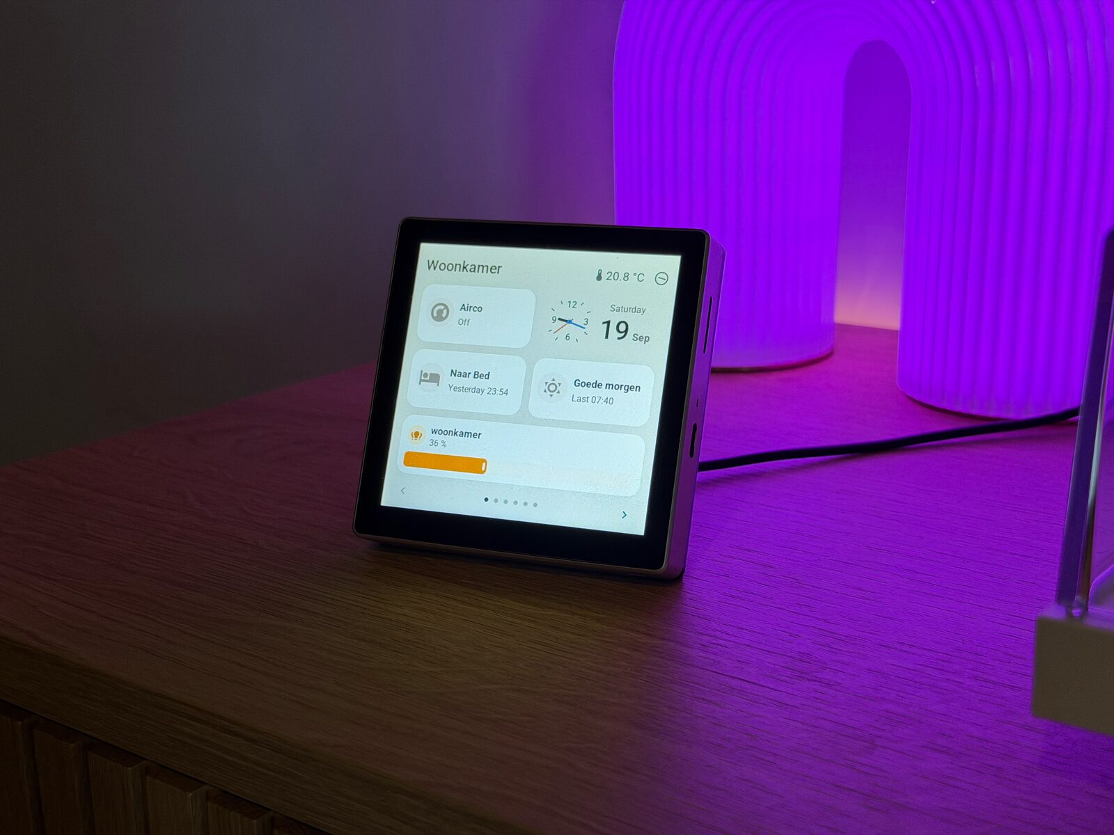 The Guition on a wooden sideboard beside a glowing purple lamp: the living room page with the airco, an analog clock with the date, two scenes and a dimmer at 36 percent