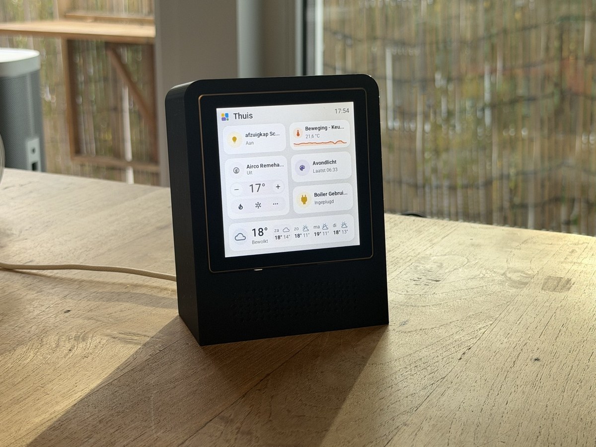 The 4-inch Guition in an upright black printed stand on a wooden table, beside a window