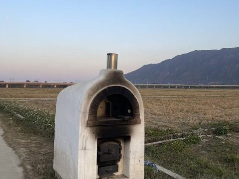 An oven at the edge of a rice paddy, a viaduct and a mountain behind
