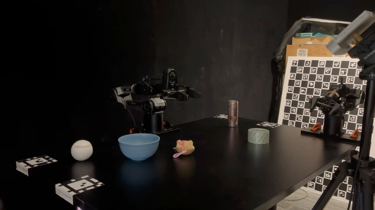 로봇 암, 다양한 소품, 마커 보드가 배치된 실험용 탁자가 보이며 VLA 기능 시연을 위한 데이터 캡처 장면이다.