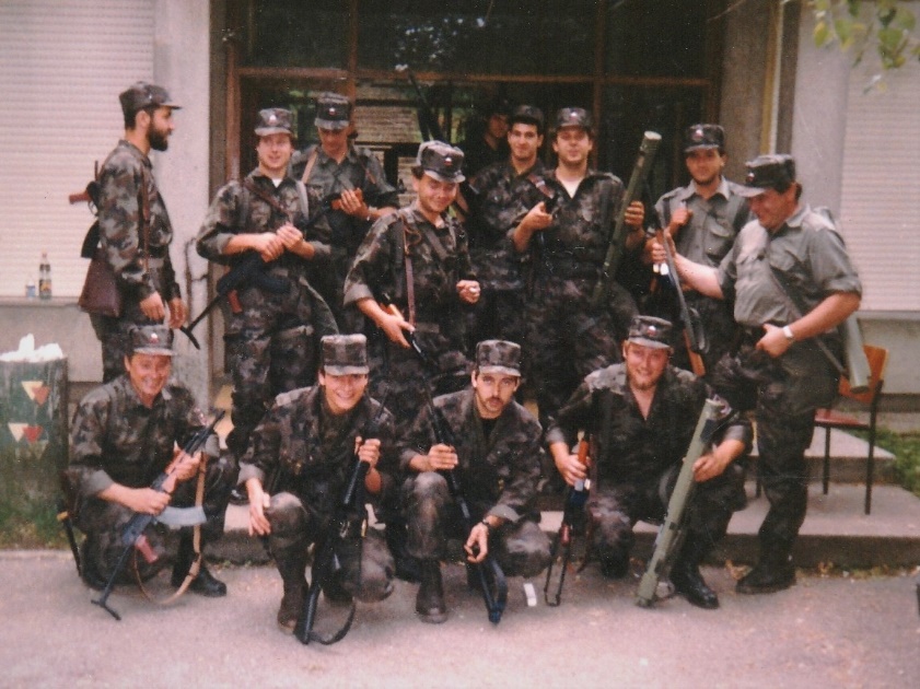 Skupaj s pripadniki voda vojaške policije, zaščitnega voda in pripadniki
                        Samostojne bojne skupine 6. Pokrajinskega štaba pred poslopjem, kjer se je
                        med vojno leta 1991 nahajal 6. pokrajinski štab za teritorialno obrambo za
                        Severno Primorsko. Mitja Močnik čepi drugi z leve proti desni.