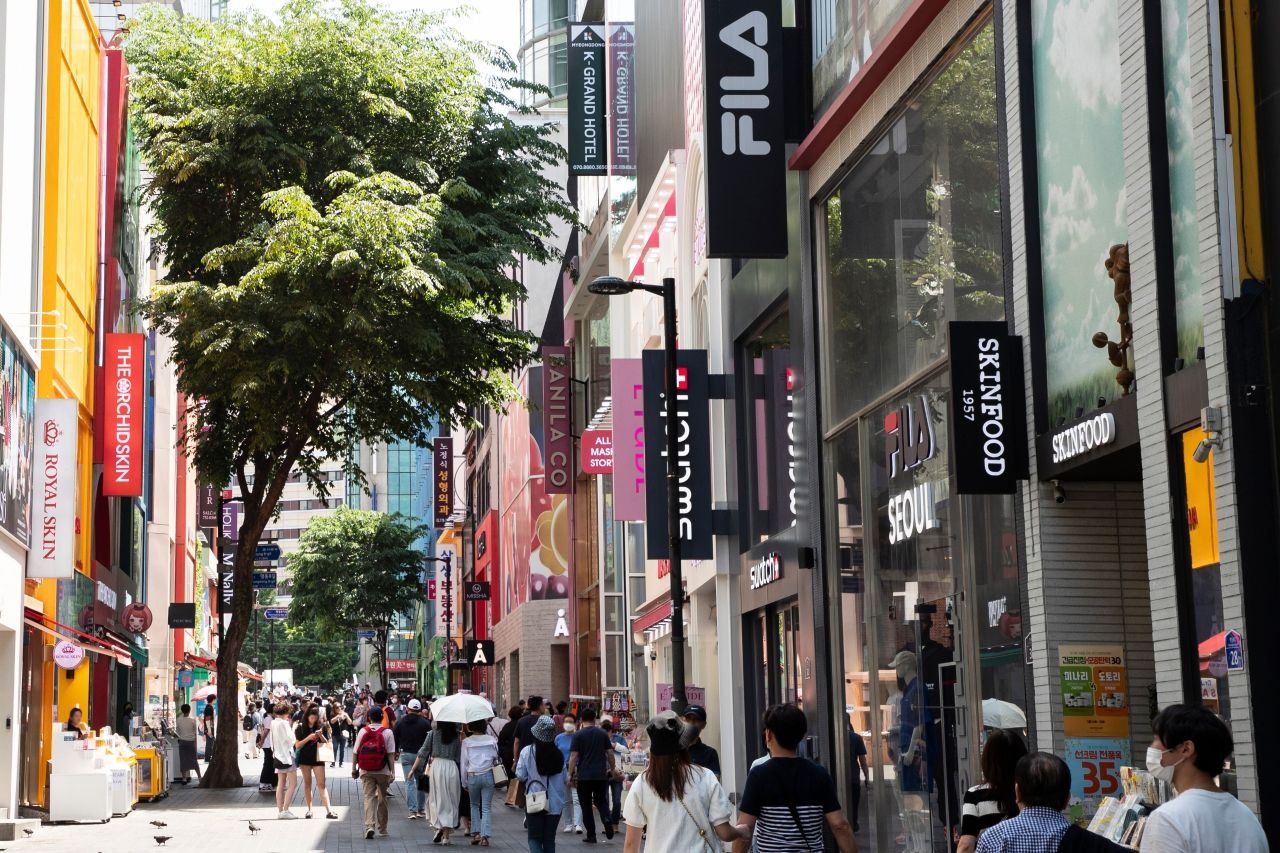 Myeongdong's cosmetics street in Seoul, Skinfood and other K-beauty storefronts lining the pedestrian lane where Olive Young-style shops sell both sun sticks (명동거리) — ⓒ한국관광공사 포토코리아-이범수 (Korea Tourism Organization, KOGL Type 1)
