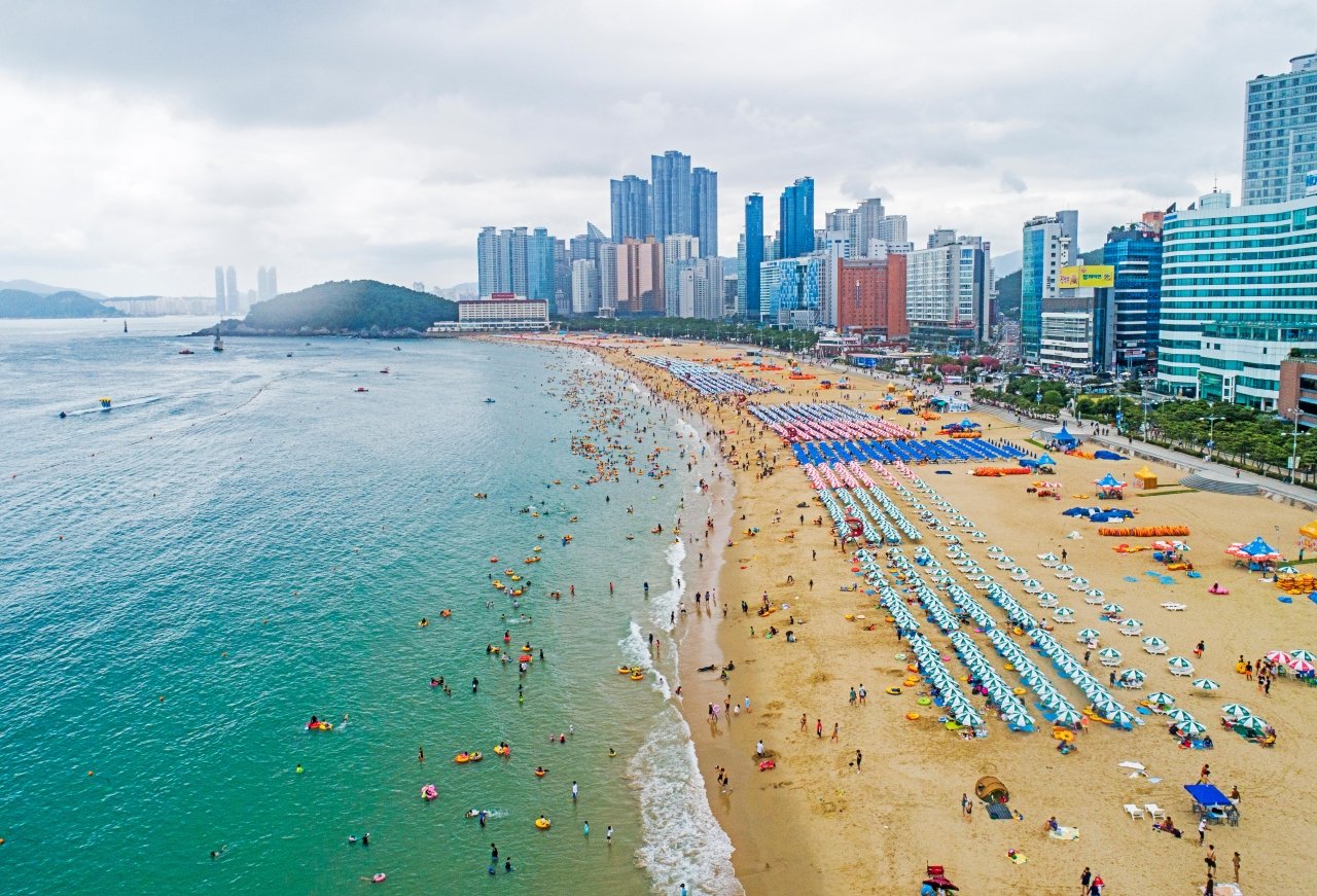 Haeundae Beach in Busan from above on a summer day, rows of parasols and swimmers in the water (해운대해수욕장) — ⓒ한국관광공사 포토코리아-라이브스튜디오 (Korea Tourism Organization, KOGL Type 1)