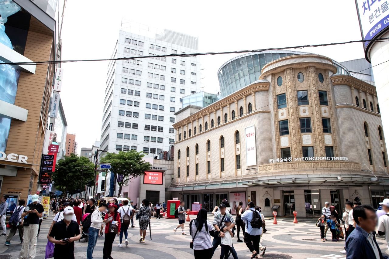 The plaza in front of Myeongdong Theater in Seoul, an All Mask Story sheet-mask shop sign visible on the left (명동거리) — ⓒ한국관광공사 포토코리아-이범수 (Korea Tourism Organization, KOGL Type 1)
