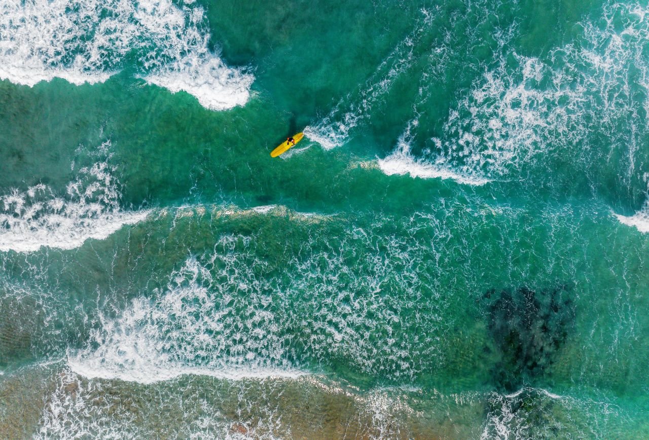 Aerial view of surf breaking on a turquoise Jeju beach with a single surfer paddling out — ⓒ한국관광공사 포토코리아-박윤준 (Korea Tourism Organization, KOGL Type 1)