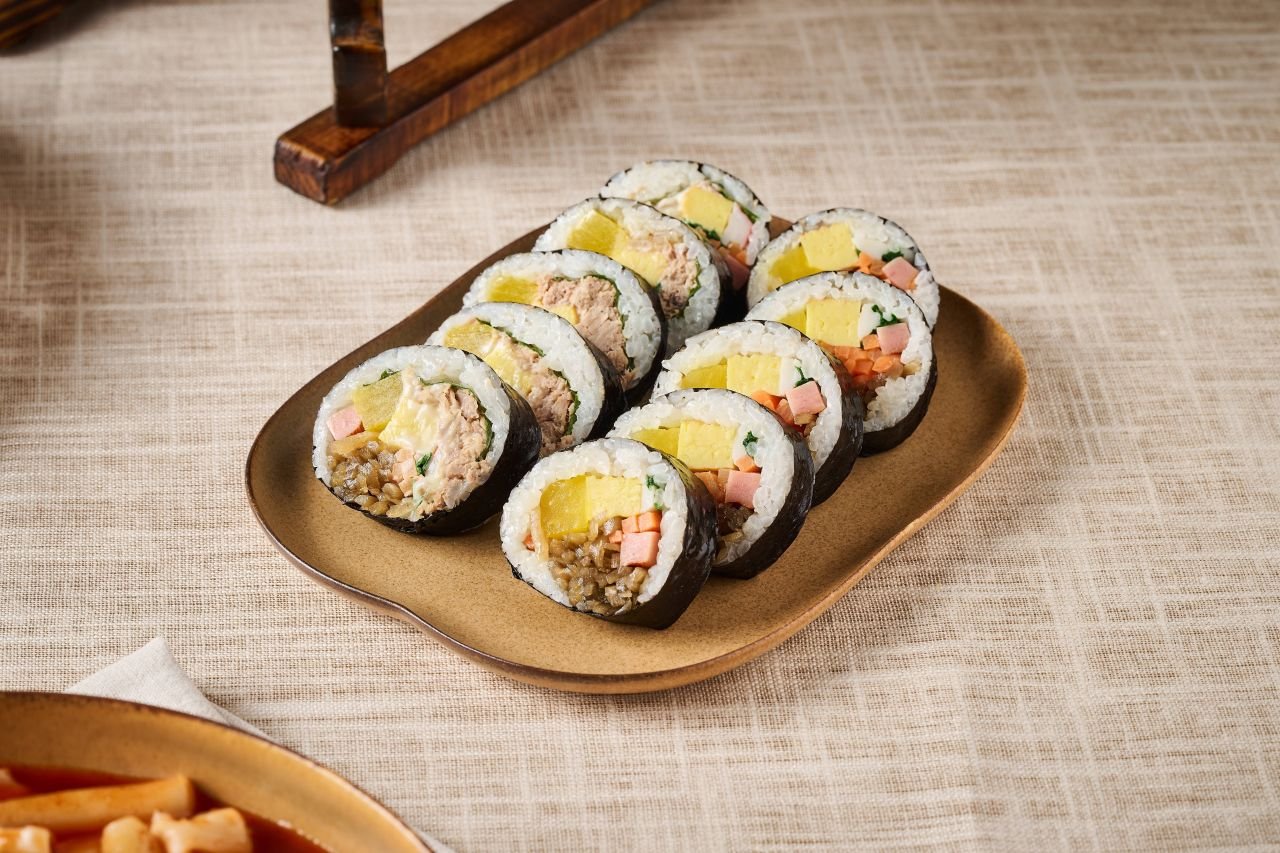 A plate of Korean gimbap rolls sliced and arranged, with tteokbokki in the corner of the frame. — ⓒ한국관광공사 포토코리아-토라이 리퍼블릭 (Korea Tourism Organization, KOGL Type 1)