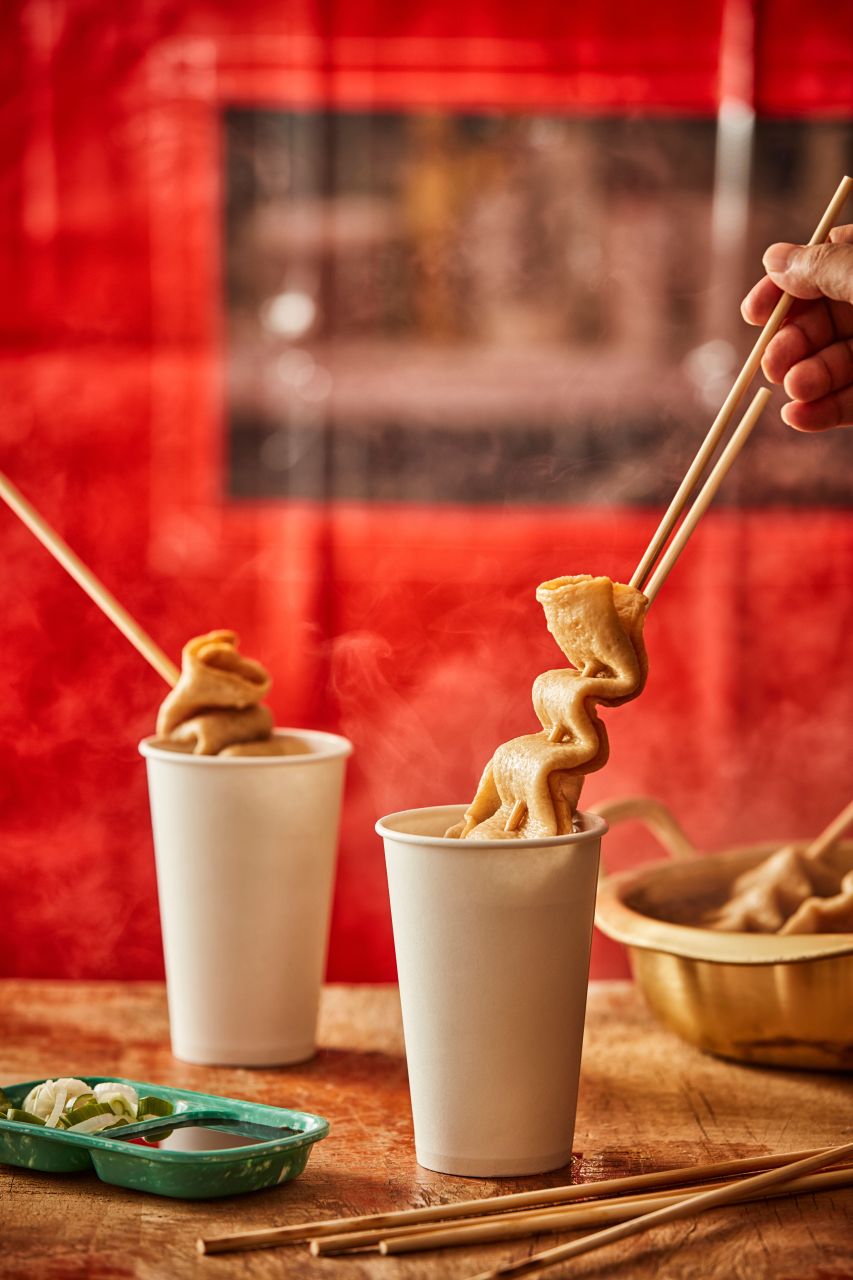 Skewers of Korean fish cake being lifted from steaming paper cups at a street food stall.