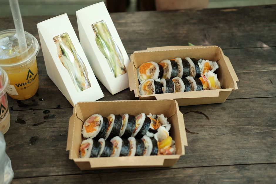 Several rolls of gimbap sliced and packed into takeout boxes on a wooden outdoor table, ready for a picnic lunch
