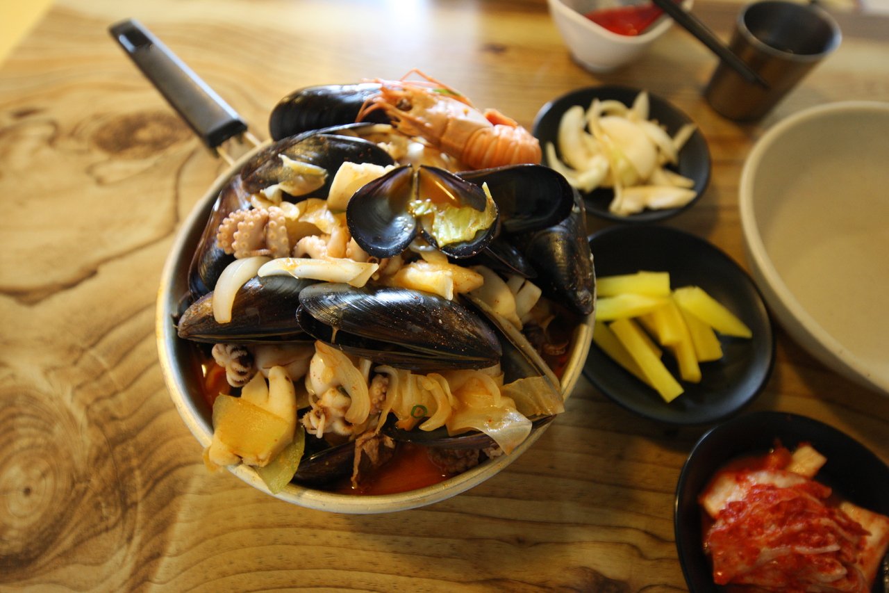 A spicy jjamppong-style seafood stew with mussels, shrimp, octopus and squid in red broth, served with sliced pickled radish and kimchi side dishes — ⓒ한국관광공사 포토코리아-김지호 (Korea Tourism Organization, KOGL Type 1)