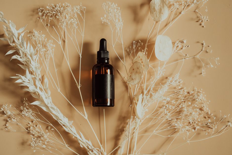 Amber glass dropper bottle for a skincare serum, styled among dried plant stems on a warm background. — Photo by Alesia Kozik on Pexels