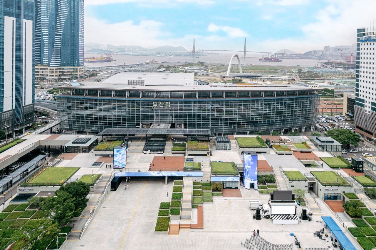 Busan Station seen from above, the glass concourse with 부산역 on the facade, and the harbor behind it. ⓒ한국관광공사 포토코리아-부산관광공사 (Korea Tourism Organization, KOGL Type 1)