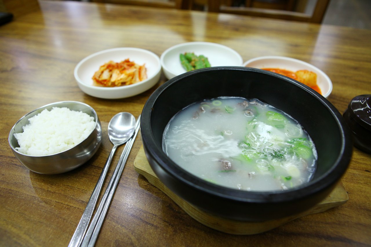 A black stone bowl of white bone broth with sliced beef and scallions, next to rice, a spoon and small side dishes. The photo's title is 곰탕 (gomtang), a related bone-broth dish and not a measured sample. Photo: ⓒ한국관광공사 포토코리아-이범수 (Korea Tourism Organization, KOGL Type 1)