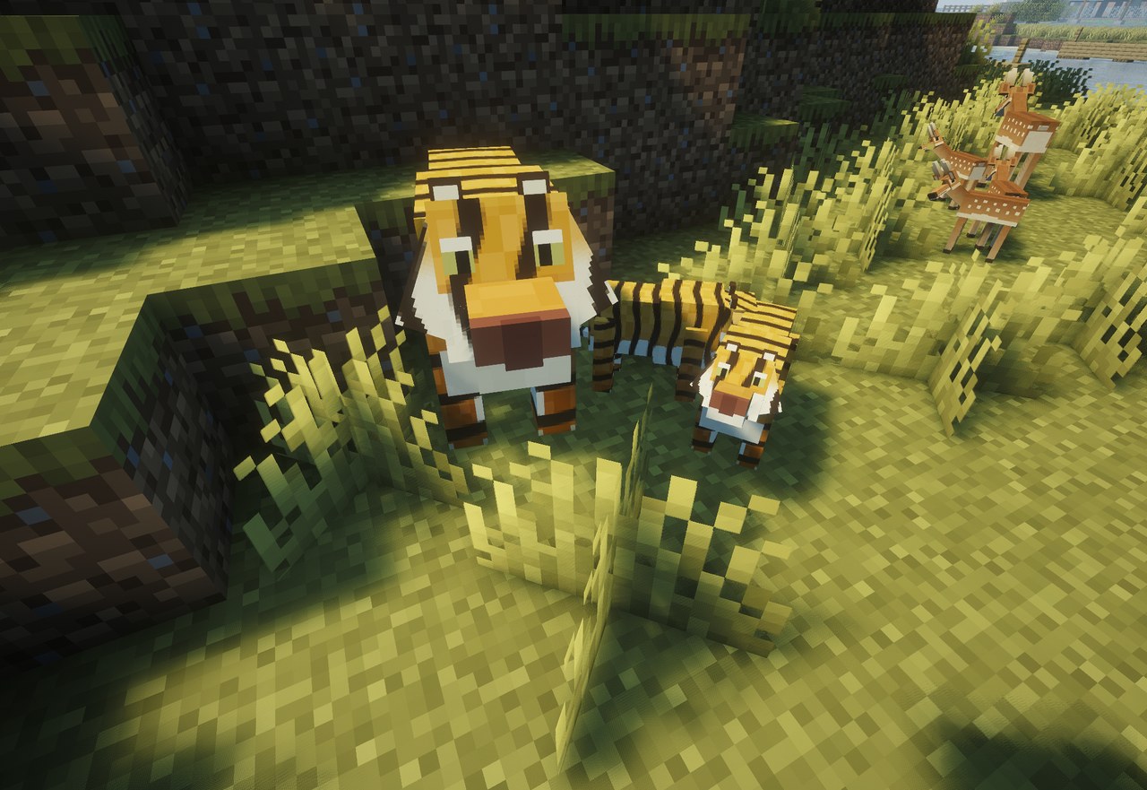 A tiger and her cub in the grass, a deer behind them