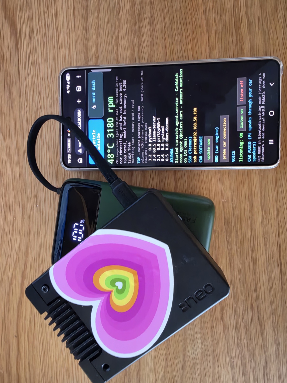 The CarWatch rig: a Raspberry Pi in a heatsink case with a heart sticker, running on a power bank, next to a phone showing the live dashboard reading 48 °C and 3180 rpm