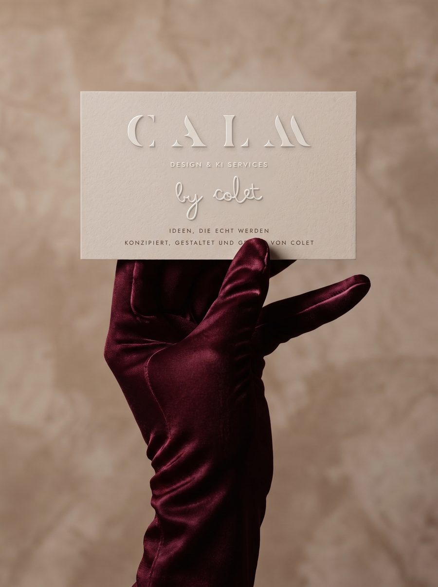 Hand im Bordeaux Handschuh hält eine geprägte Visitenkarte von CALM Design & KI Services by colet