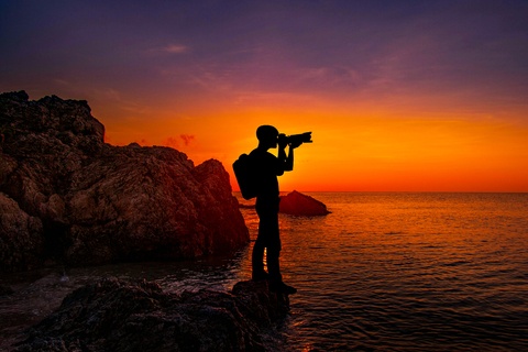 A man standing on a beach with a camera at dusk