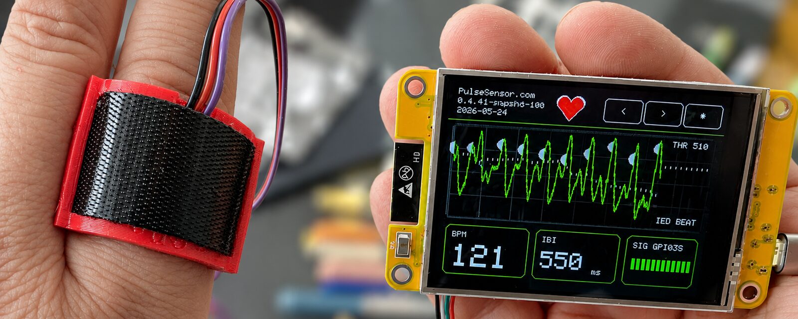 PulseSensor CyberDeck running 1.3.0-launch firmware on an ESP32-2432S028 — live waveform reading 121 BPM next to a finger wearing a red 3D-printed PulseSensor ring