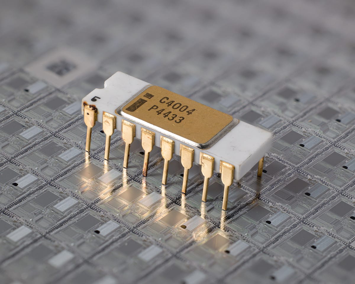Intel C4004 processor, three-quarter view on a silicon wafer: white ceramic 16-pin DIP, gold lid 'i C4004 P4433', gold pins