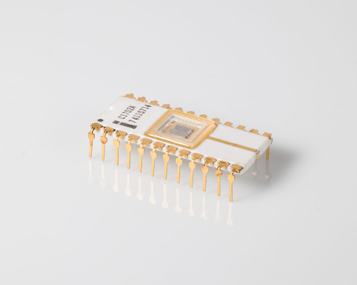 Intel C1702A EPROM, three-quarter view: white ceramic 24-pin DIP, quartz window over the die, 'C1702A 7411S714', gold pins