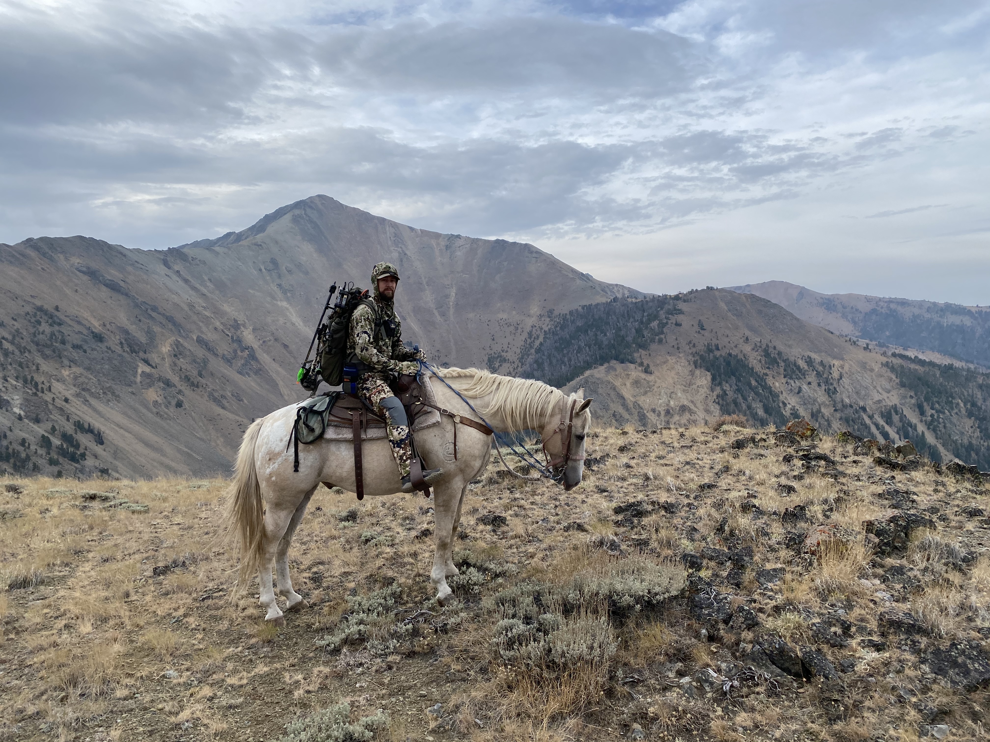Zach on horseback on a mountain ridge, bow on his pack