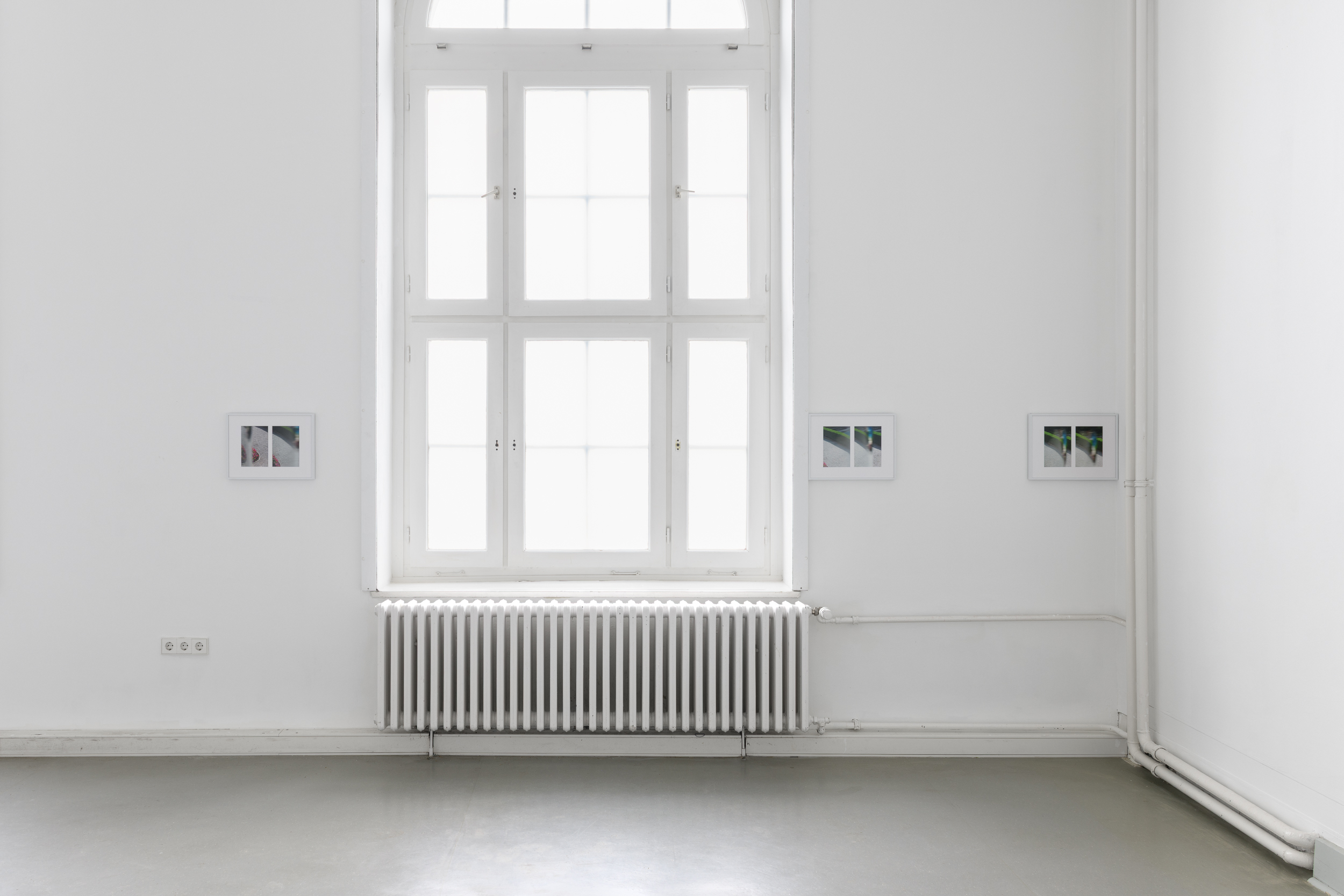 Aisha Altenhofen, The Carrier at UdK Berlin: Installation view of three photographic works arranged asymmetrically around a large arched window and radiator.