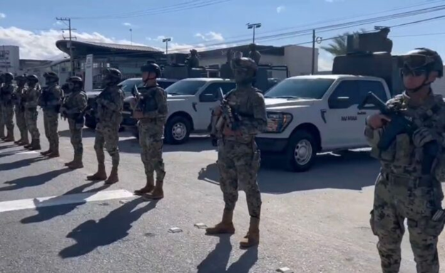 Personal militar resguarda una zona con vehículos oficiales mientras se forma en línea durante un operativo de seguridad