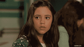 A girl reacts thoughtfully in a busy classroom setting.