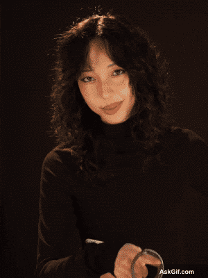 A girl with curly hair smiles confidently in a dimly lit setting.