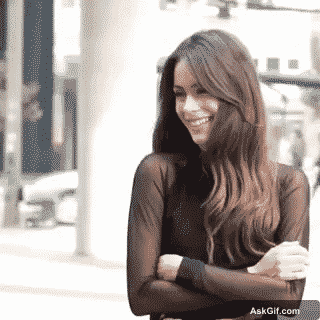 A woman smiles while posing confidently in a stylish outfit.