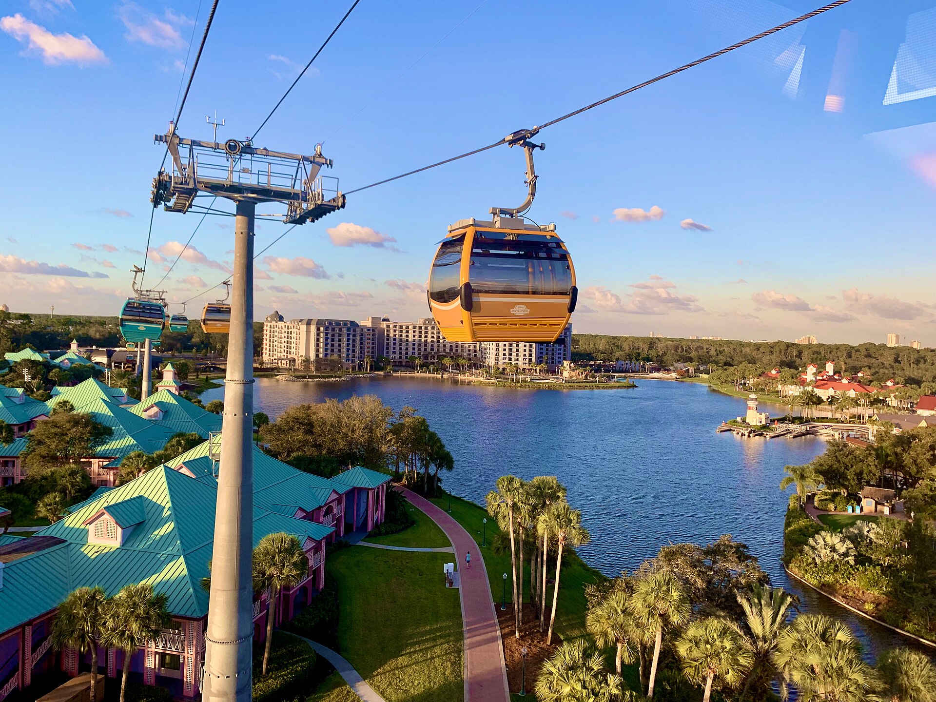 Disney Skyliner gondolas cross Crescent Lake at golden hour, with Disney's Caribbean Beach Resort below and Disney's Riviera Resort across the water at Walt Disney World.