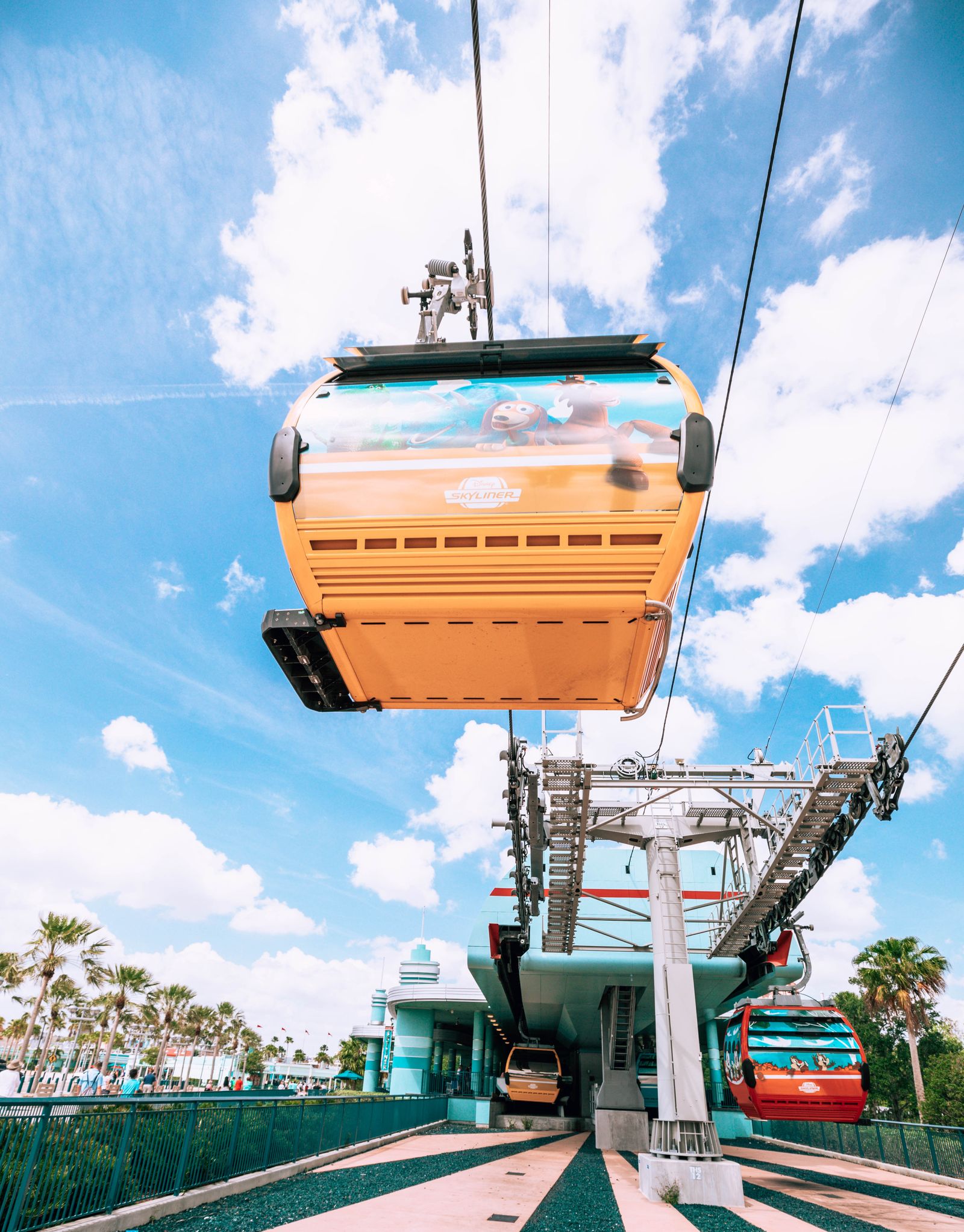 A Disney Skyliner gondola wrapped with Toy Story characters passes overhead at the Hollywood Studios station.