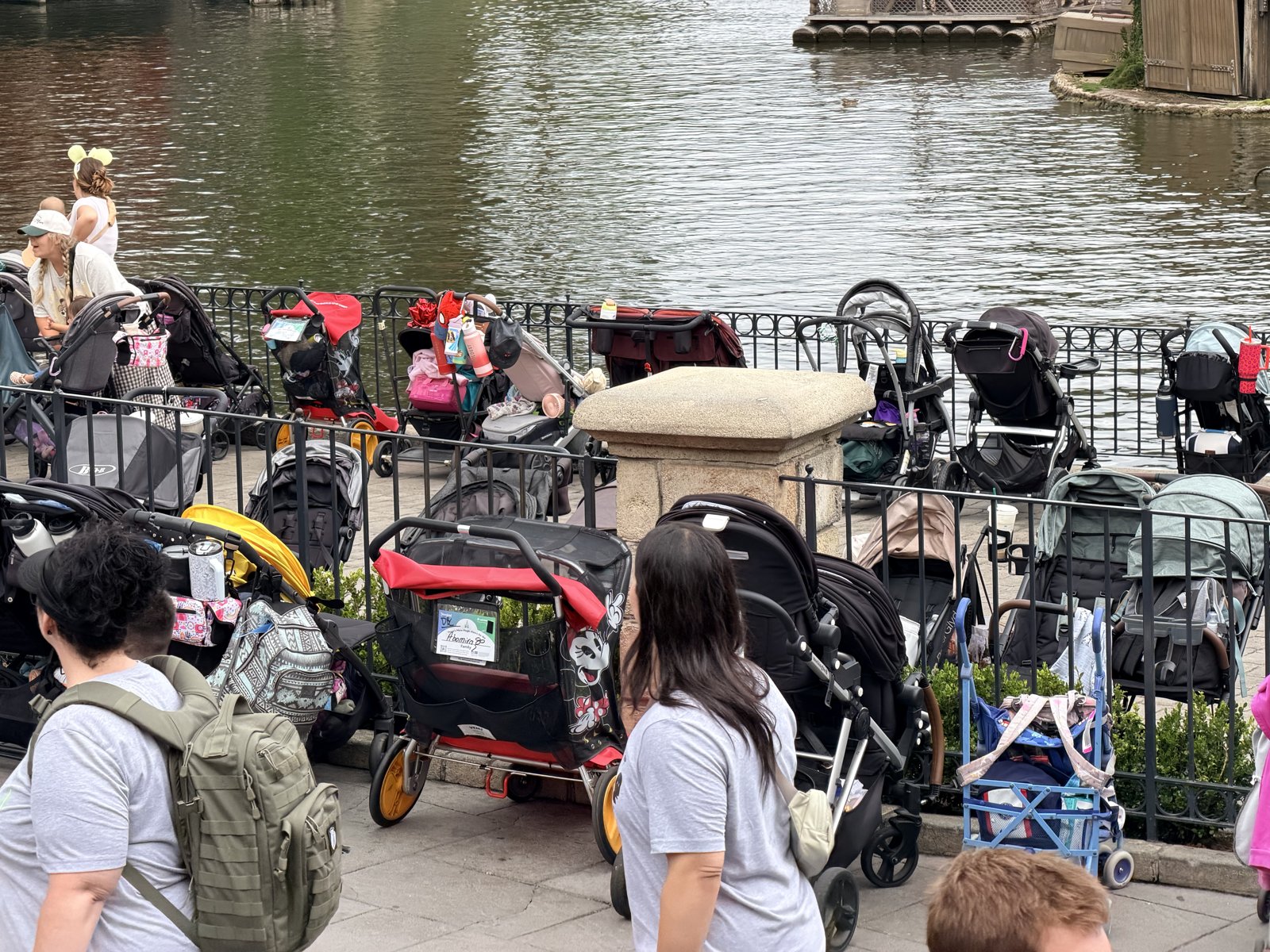 Rows of parked strollers fill a stroller parking area along a riverfront railing in a Disney park.