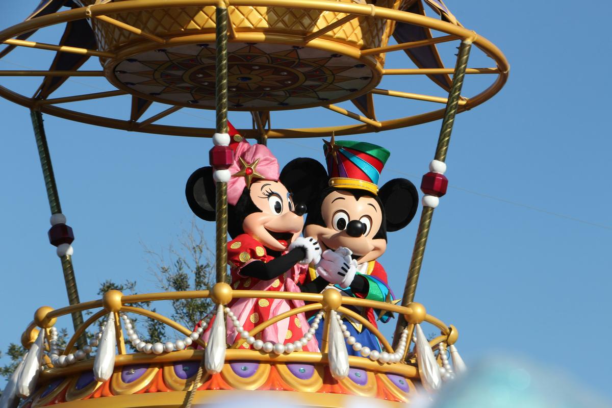 Mickey and Minnie Mouse in festive costumes on a parade float at a Disney theme park