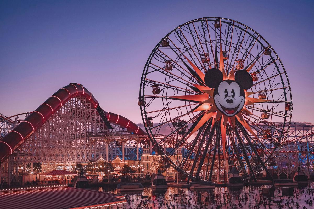 Pixar Pier at Disney California Adventure at dusk with the Mickey ferris wheel and Incredicoaster lit up against a purple sky