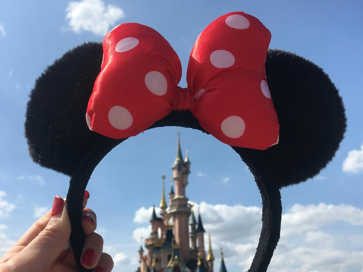 Minnie Mouse ears headband held up in front of a Disney castle on a sunny day