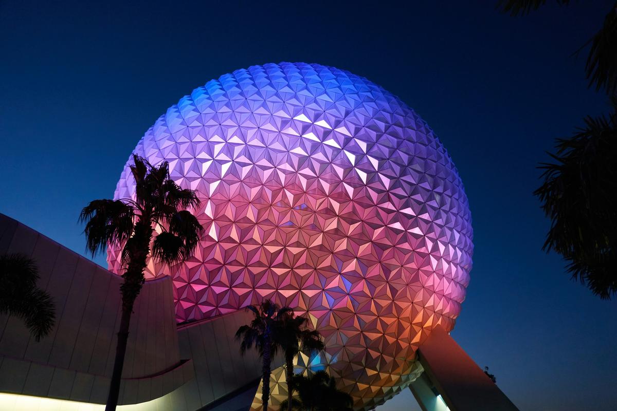Spaceship Earth at EPCOT illuminated in purple and pink at night with palm tree silhouettes
