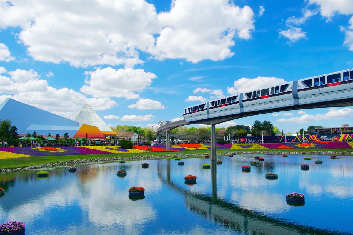 Walt Disney World monorail passing over the EPCOT lagoon surrounded by colorful flowers on a sunny day