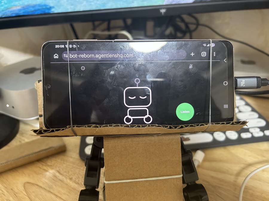 A phone held on the headless robot by a cardboard saddle and rubber bands, showing the robot's face